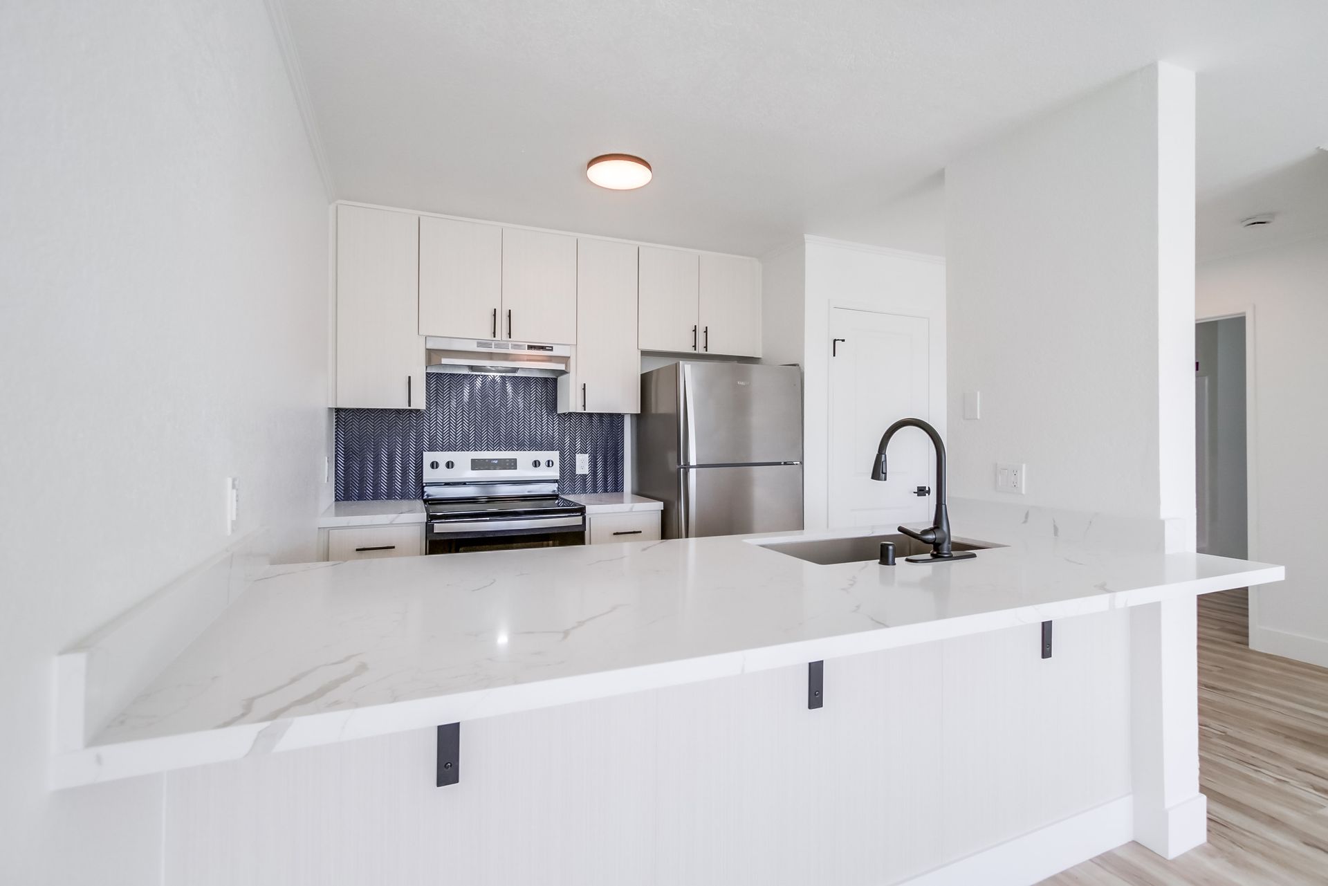 White kitchen with marble countertop, stainless steel appliances, and blue tile backsplash.