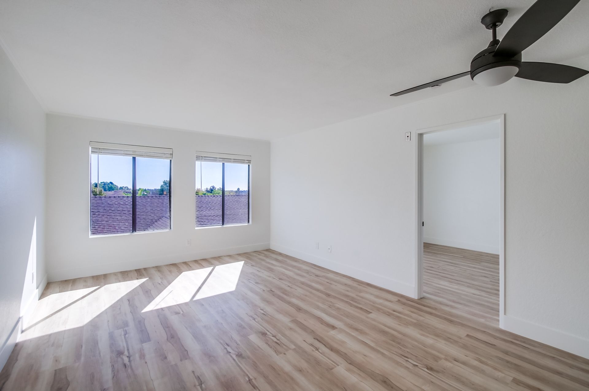 Empty room with wood-look floor, white walls, two windows, and a ceiling fan.