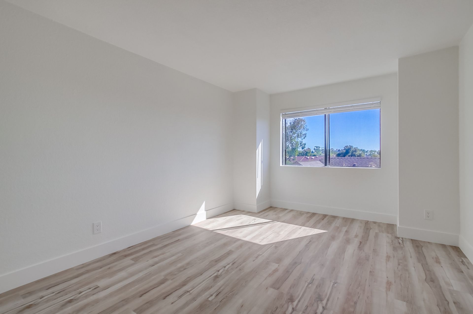 Empty room with white walls, wood-look floor, and window with a view.