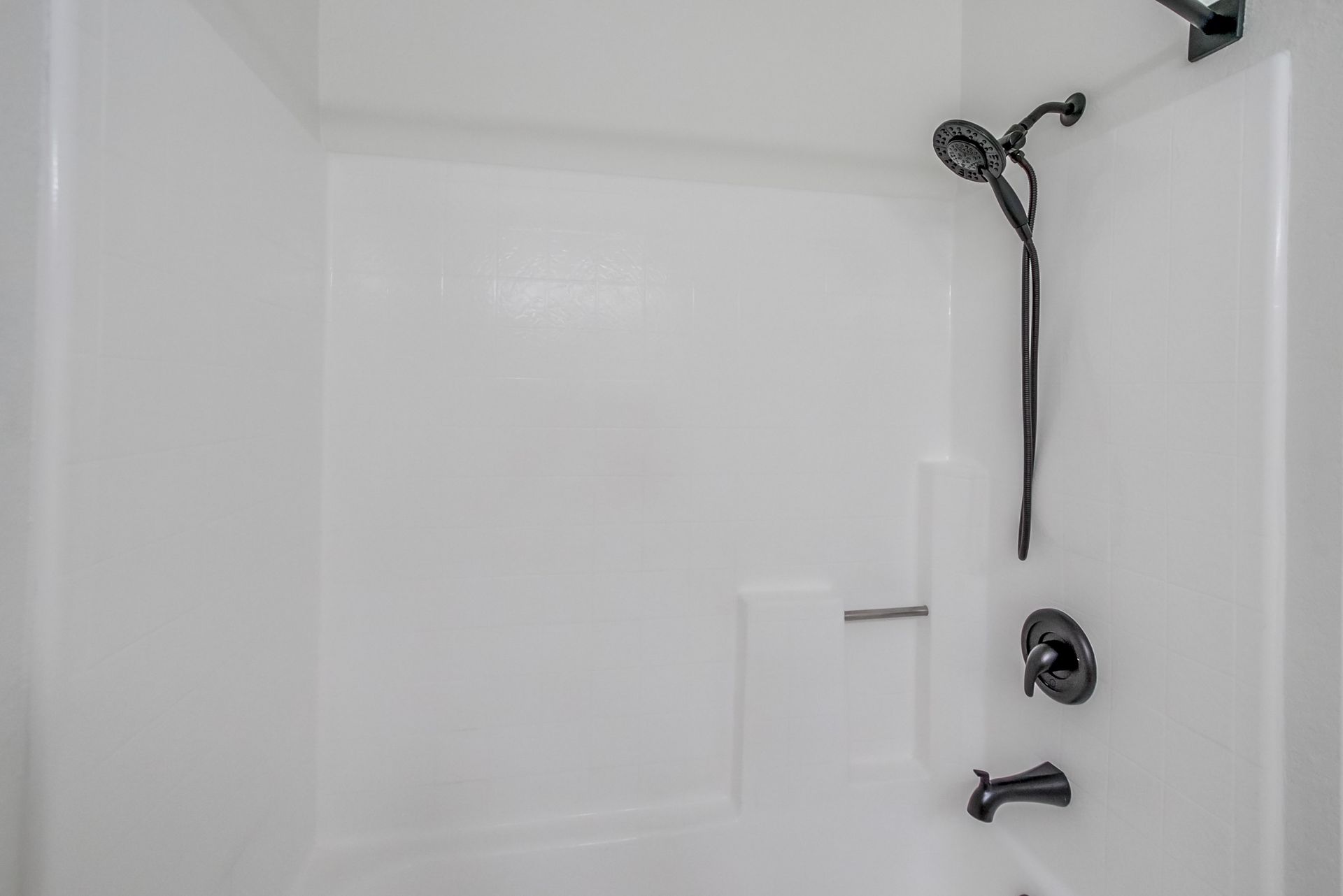 White shower stall with black showerhead, faucet, and hardware.