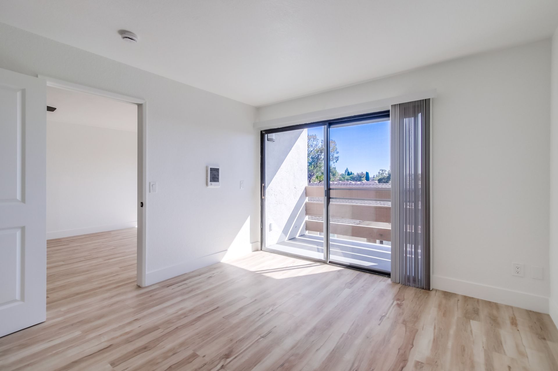 Empty room with light wood floors, sliding glass door to balcony. White walls and door frame.
