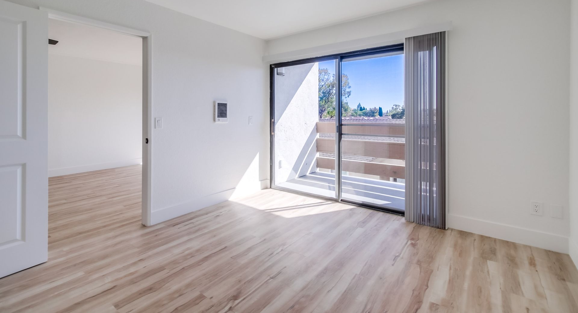Empty room with wood-look floors, a sliding door to a balcony, and a doorway to another room.