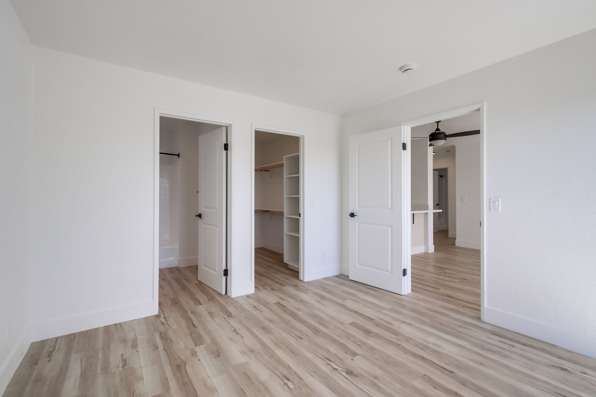Empty room with three white doors, wood floors, and white walls.