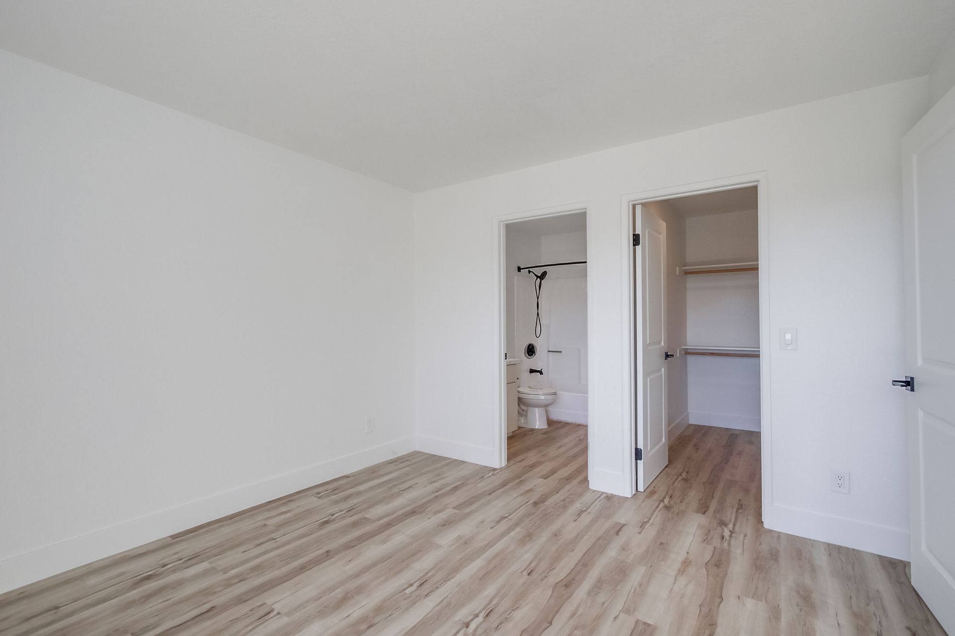 Empty bedroom with light wood floors, white walls, and two open doorways.