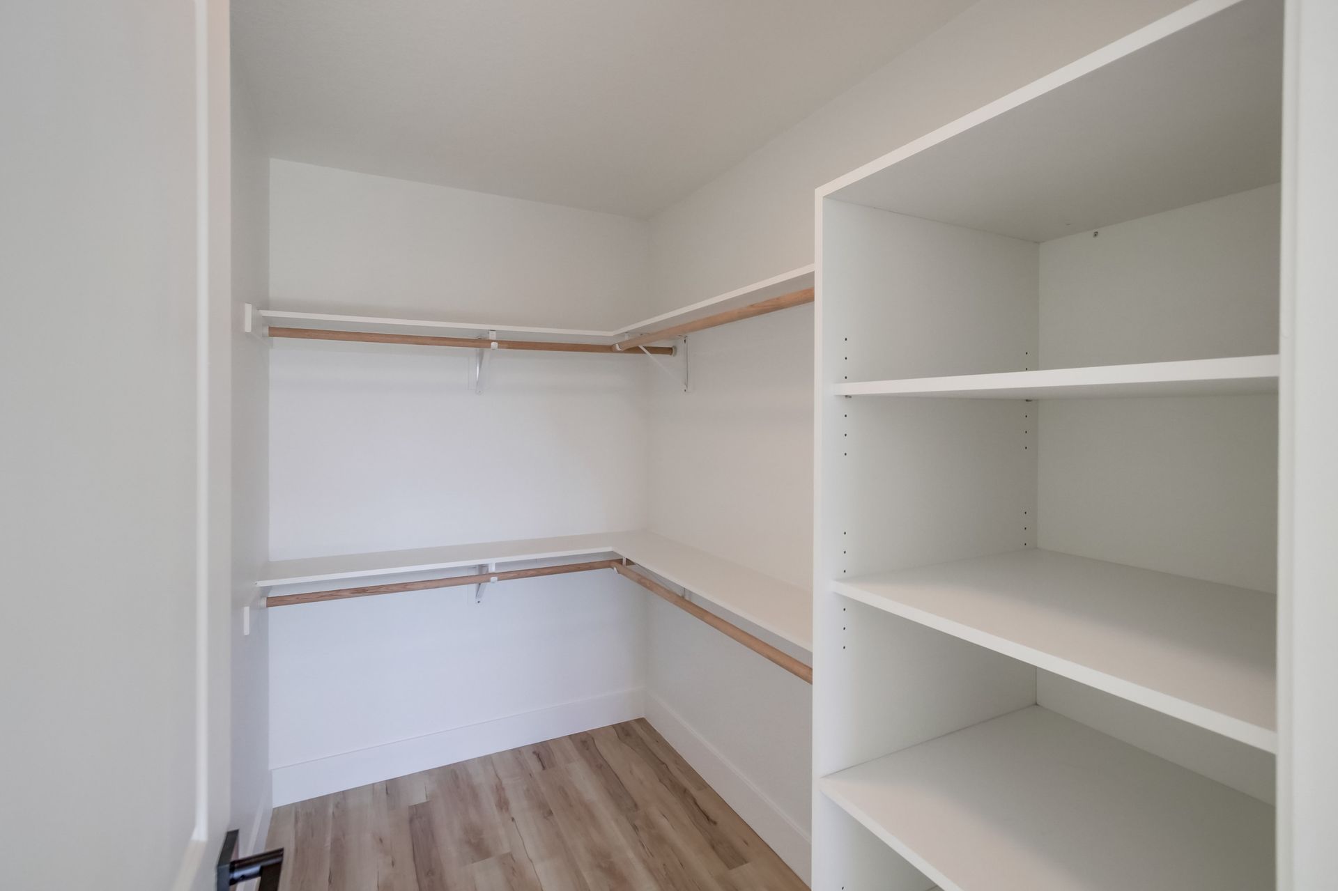 Empty walk-in closet with white shelves, clothing rods, and light wood flooring.