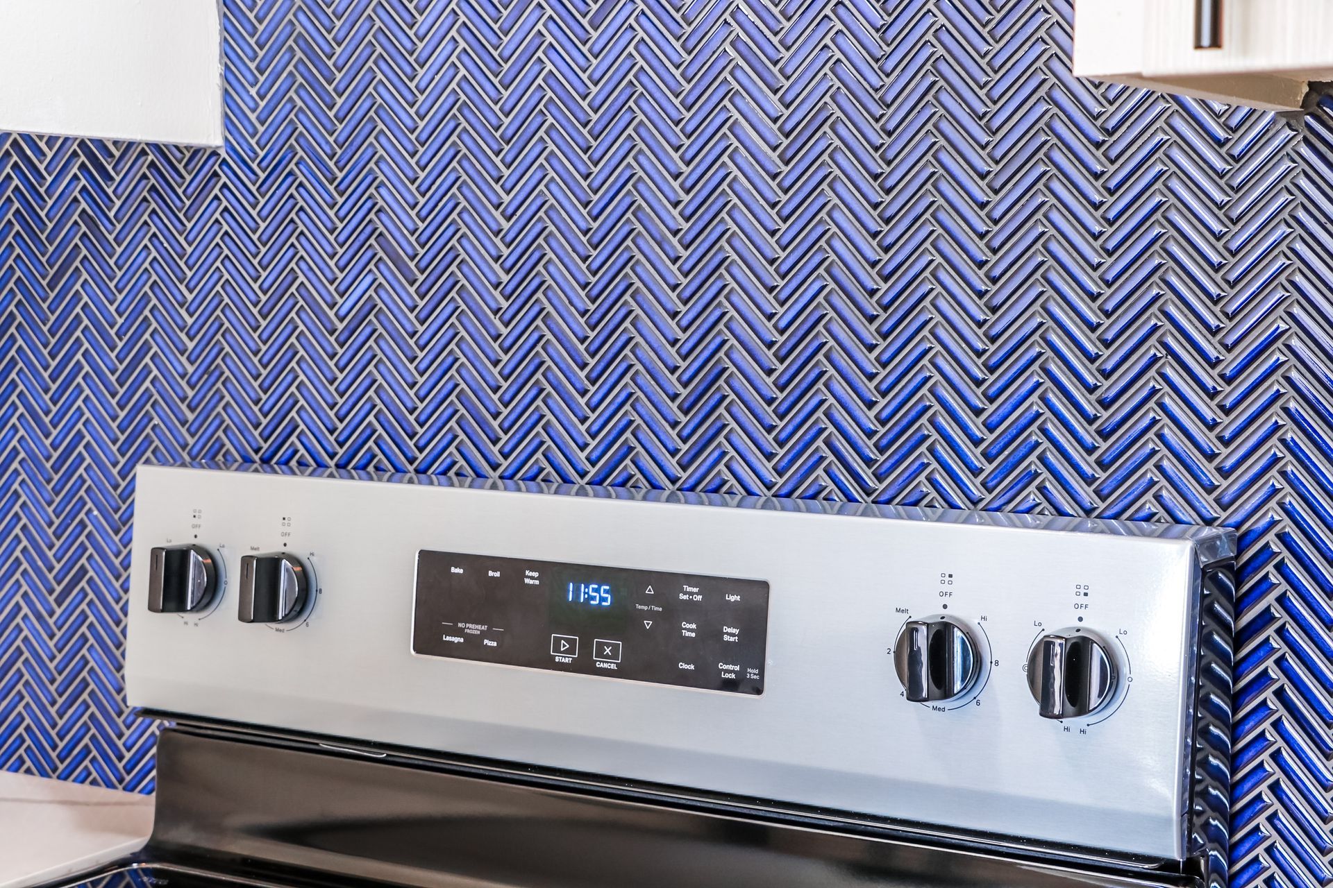 Electric stove with silver controls against blue herringbone tile backsplash.