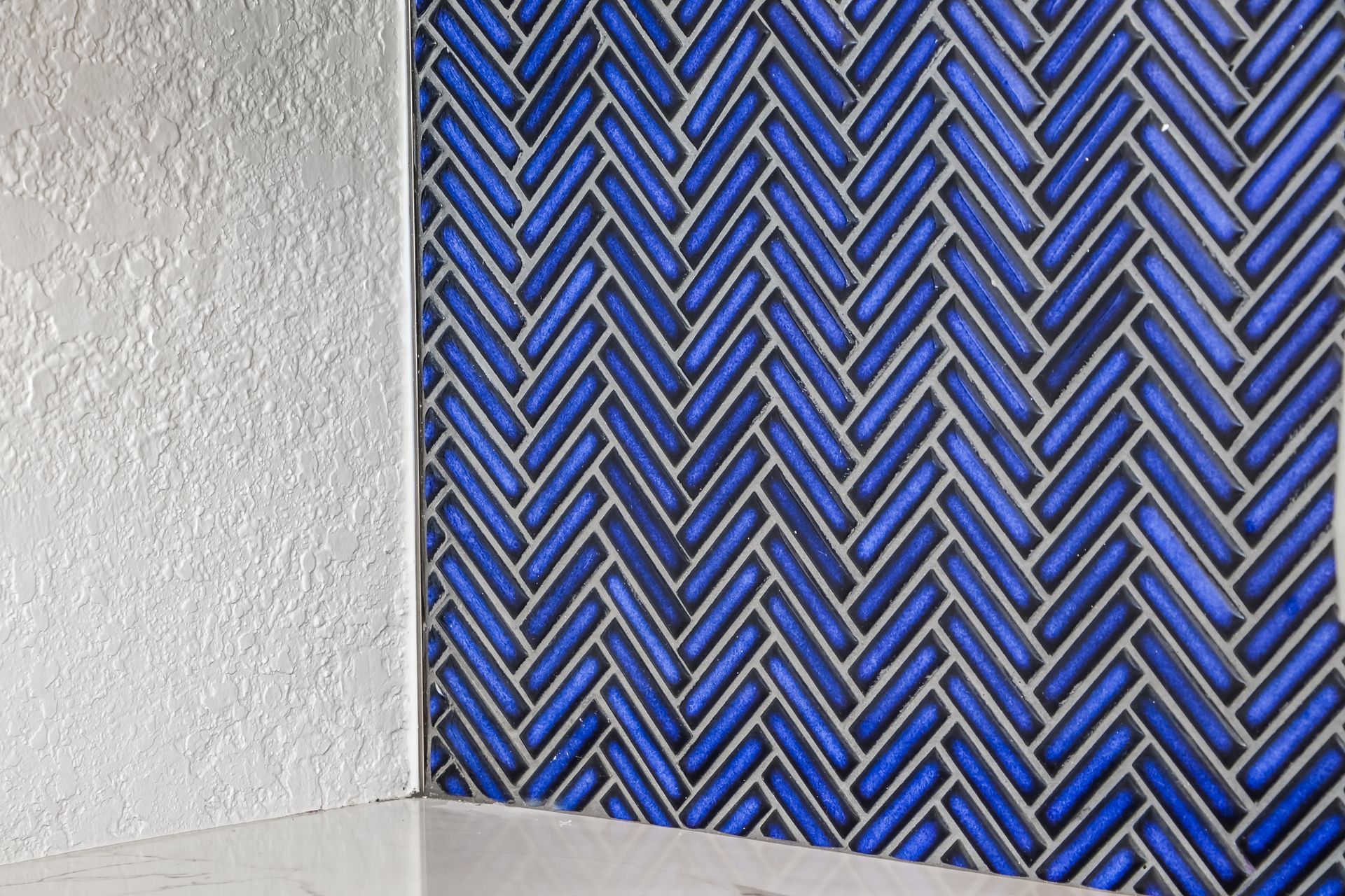 Blue herringbone tile wall meets a white textured wall.