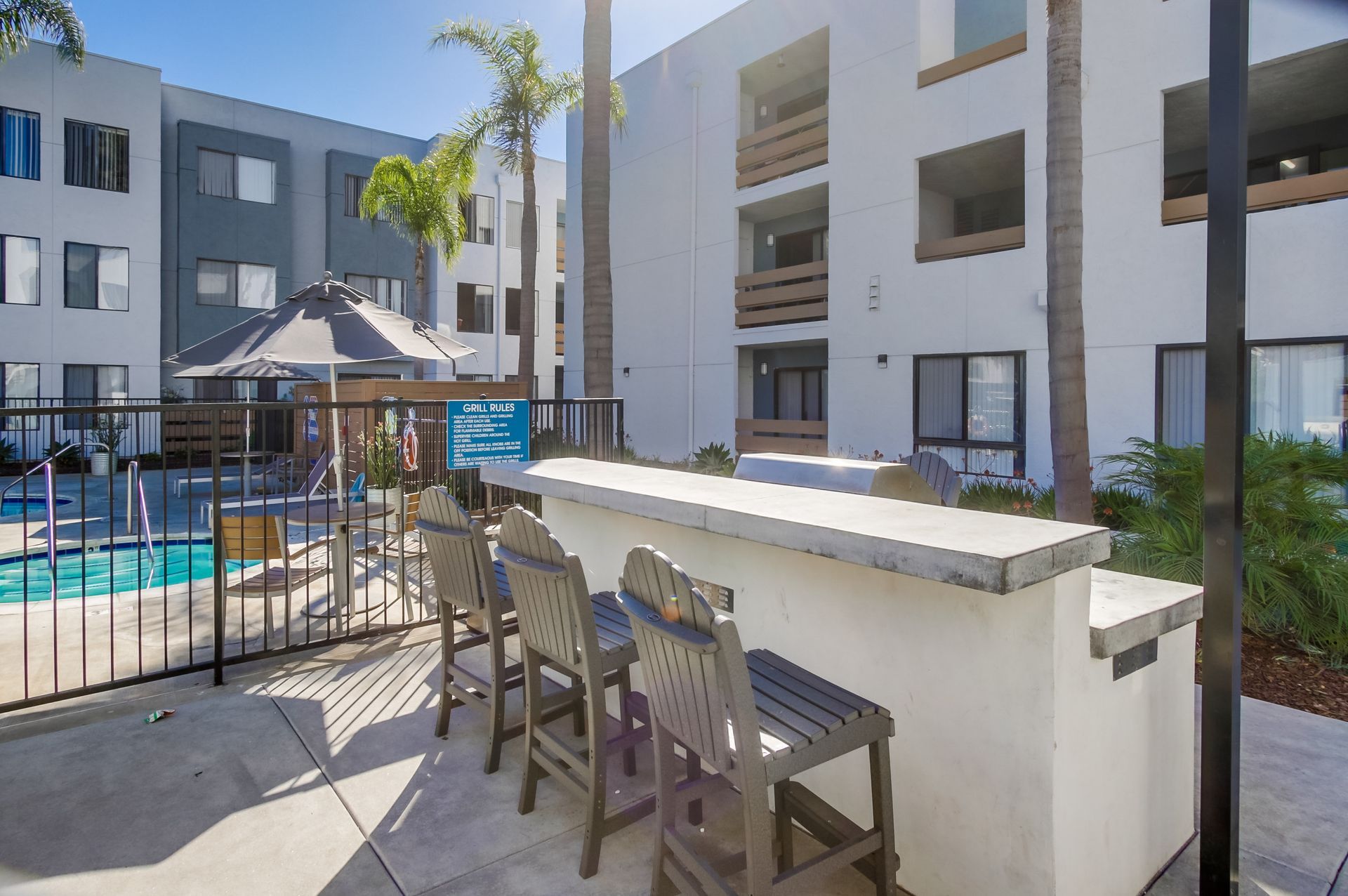 Outdoor bar area with stools, pool, and apartment buildings.