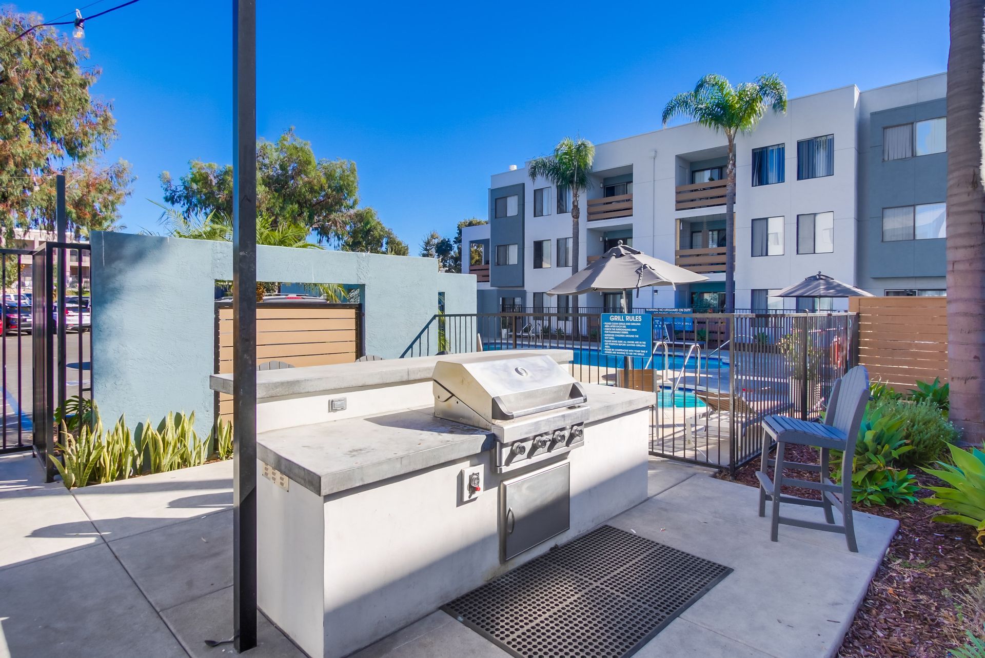 Outdoor grilling station with a concrete countertop, near a pool and apartment building.