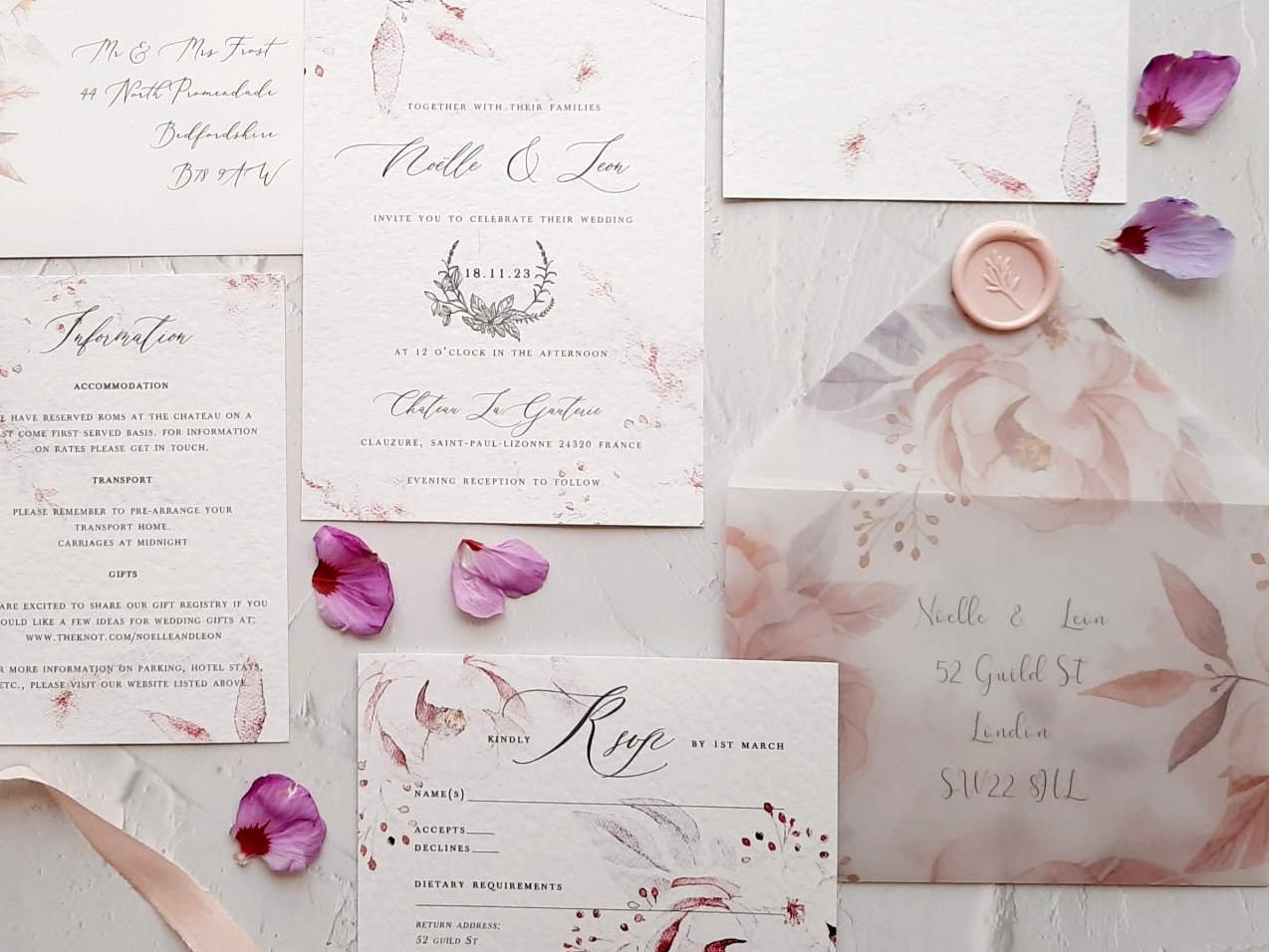 A wedding invitation and envelope with purple petals on a table.