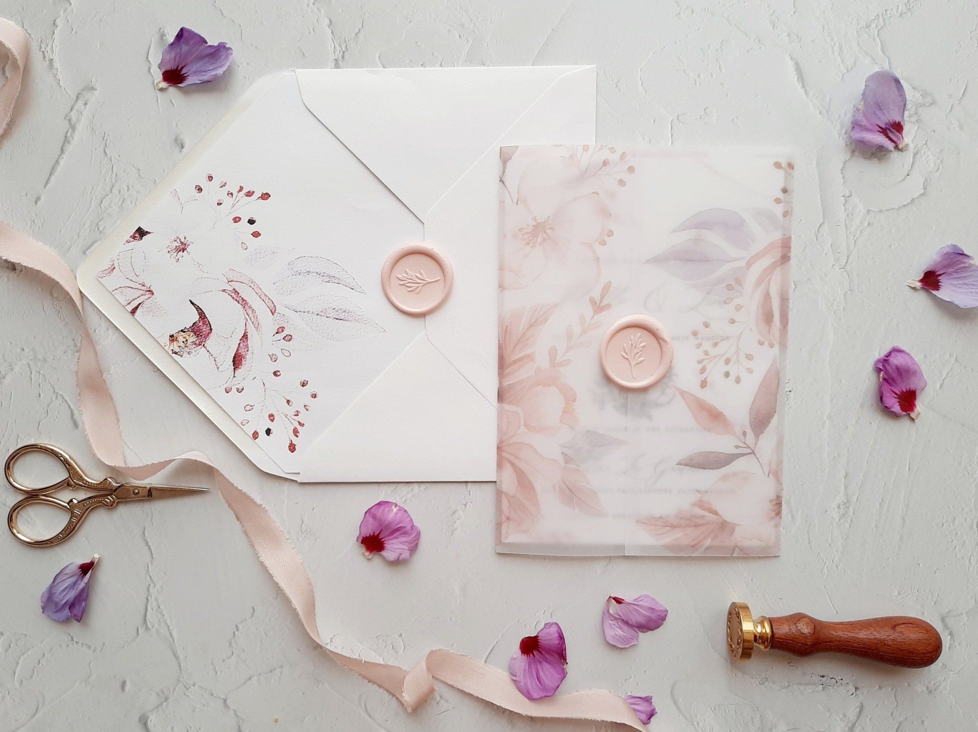 A wedding invitation , envelope , wax seal , scissors and flowers on a table.