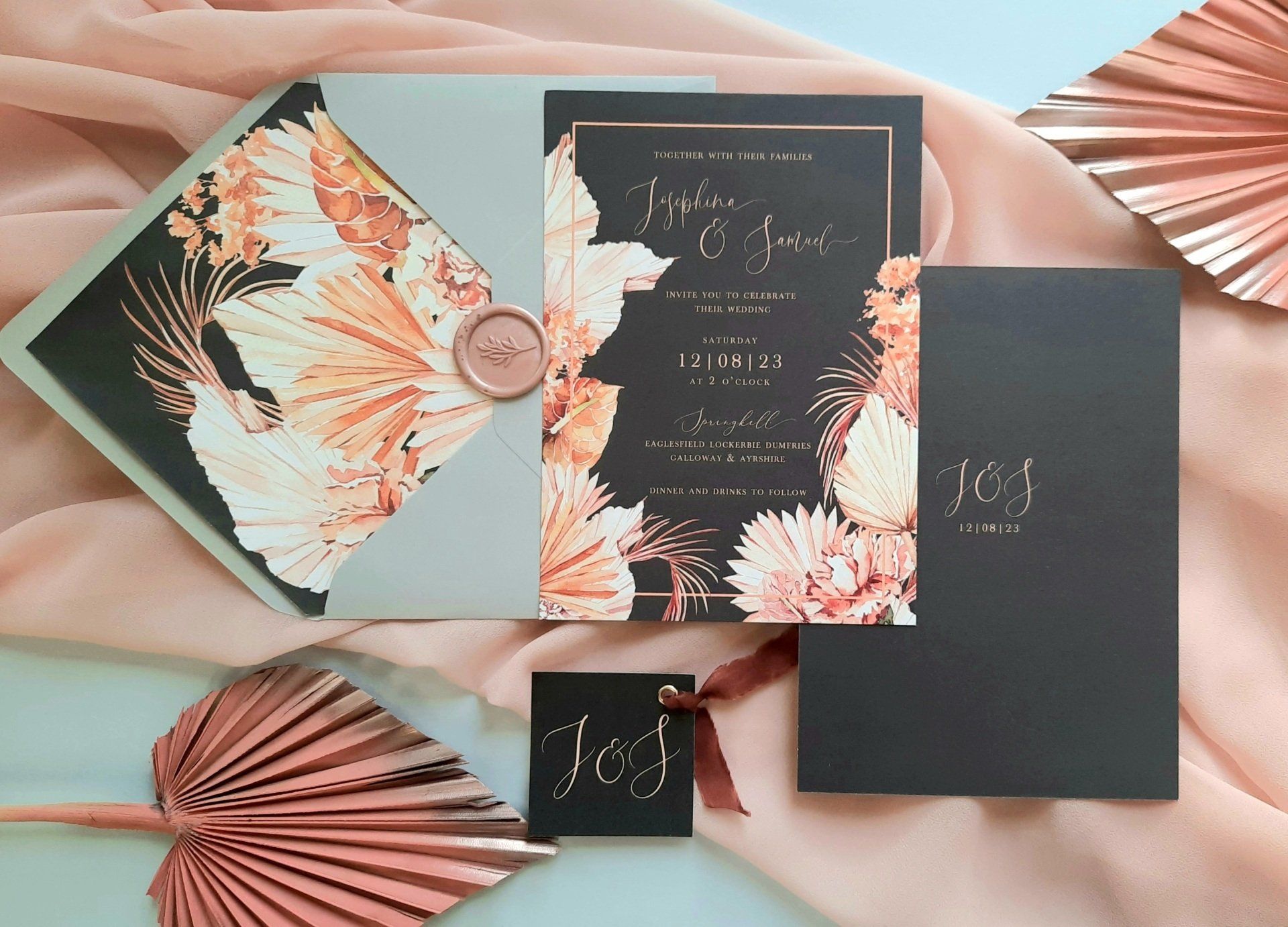 A wedding invitation is sitting on a table next to a fan.
