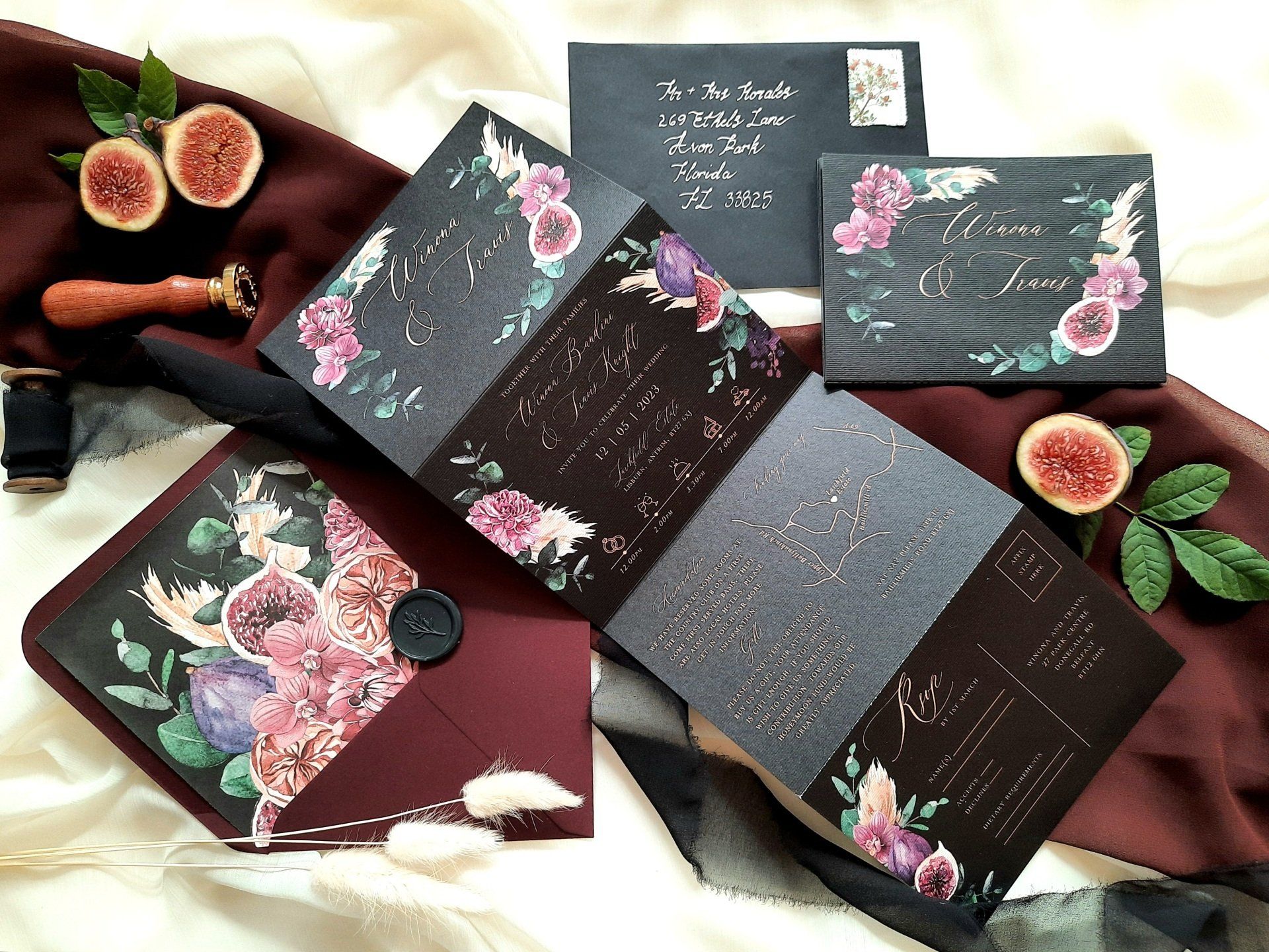 A black wedding invitation with purple flowers and figs are sitting on a table.