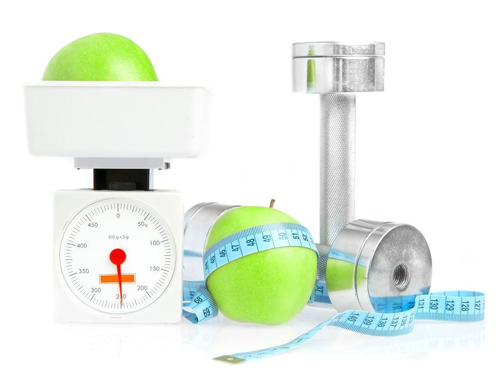 A green apple is on a scale next to a measuring tape and a dumbbell featuring health and fitness deals online