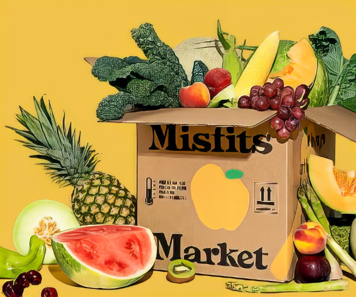 A box of Misfits Market produce overflowing with fruits and vegetables on a yellow background.