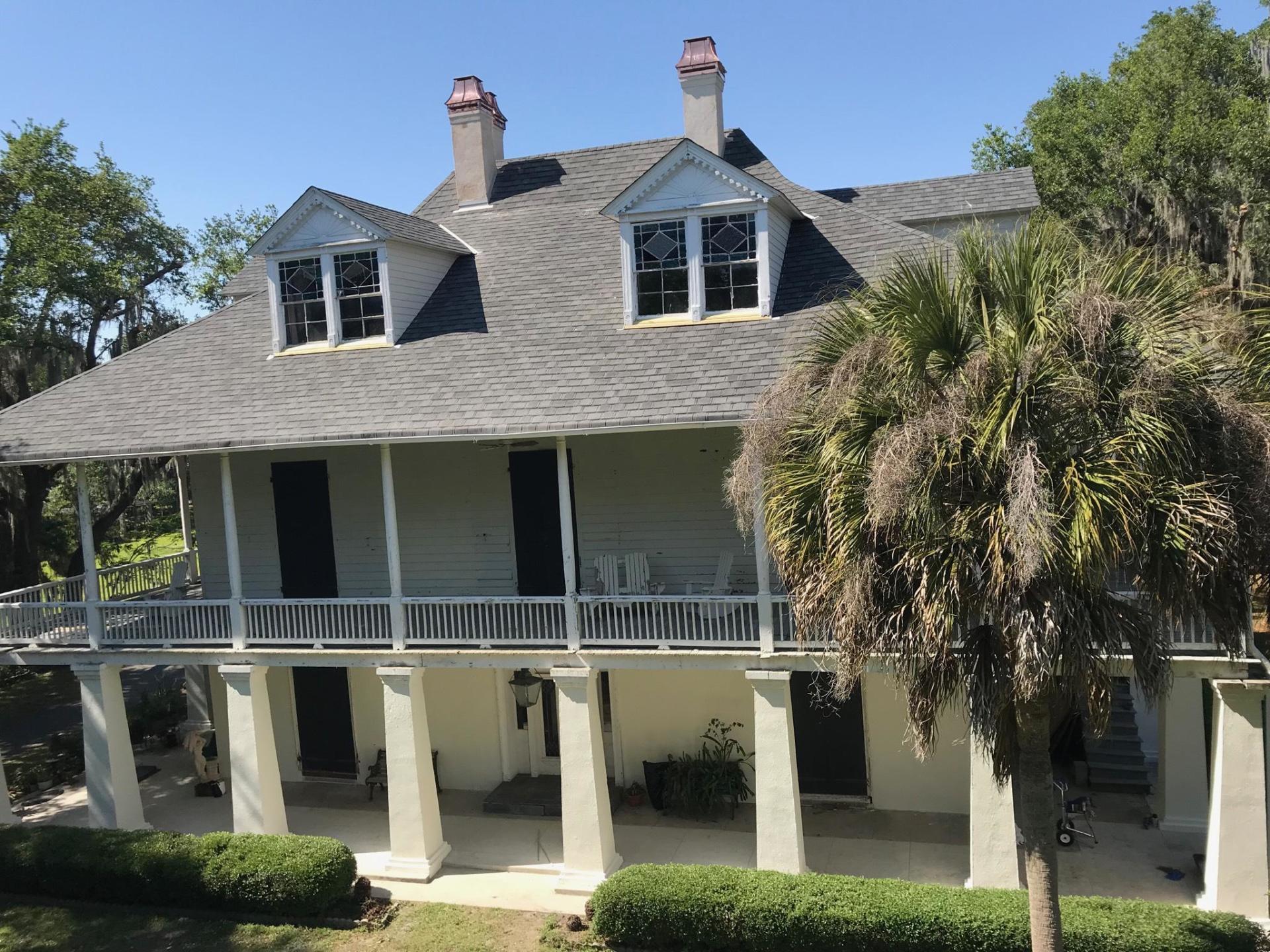 Two-story white house with a porch, supported by pillars, under a blue sky; palm tree in the foreground.