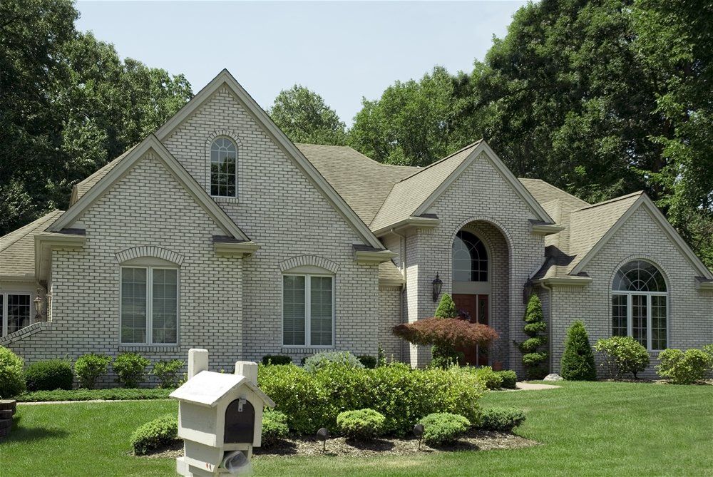 Brick house with a light-colored facade and dark roof, set in a green lawn with shrubs and a mailbox.