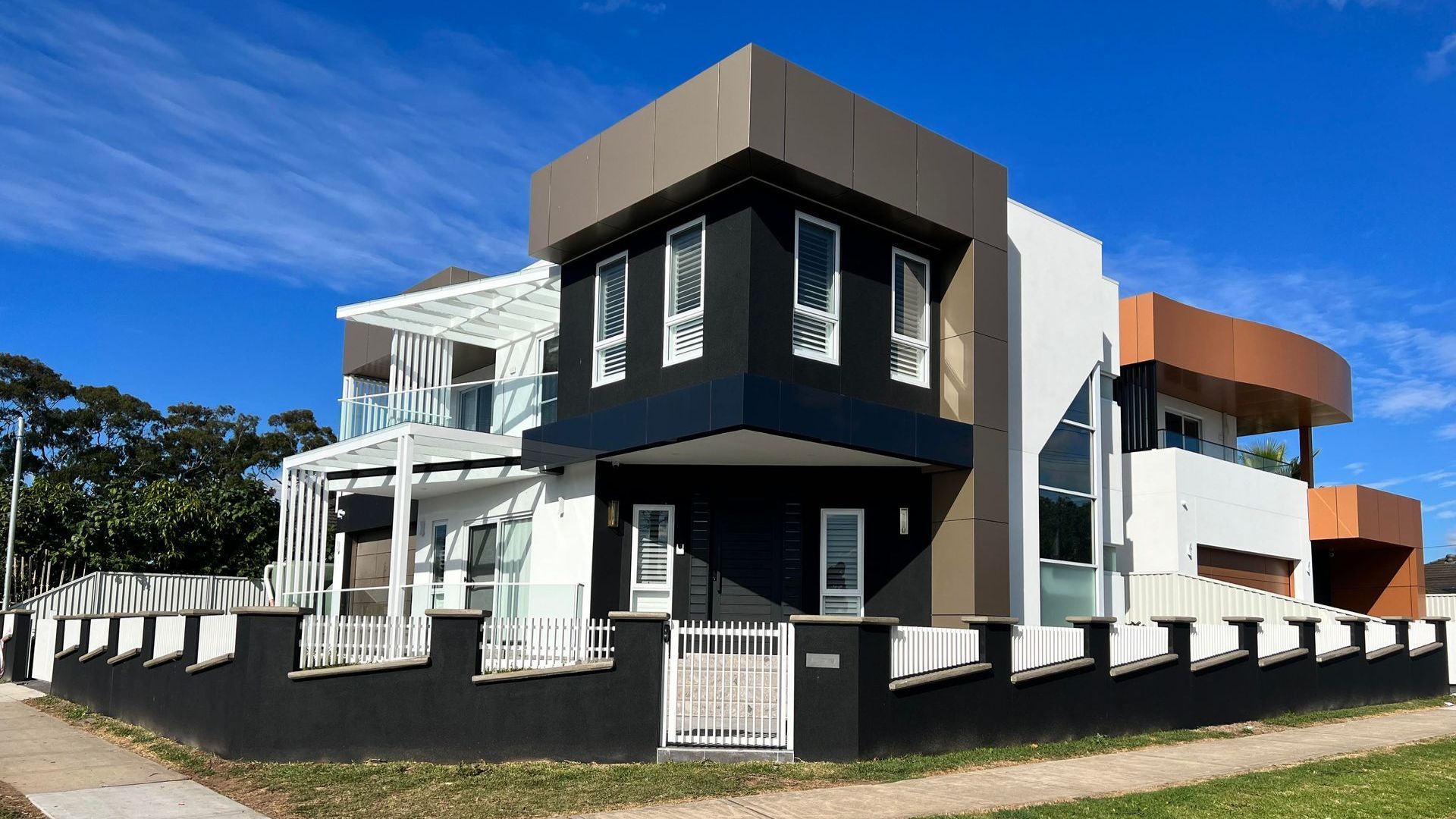 A large modern house with a black and white fence in front of it.