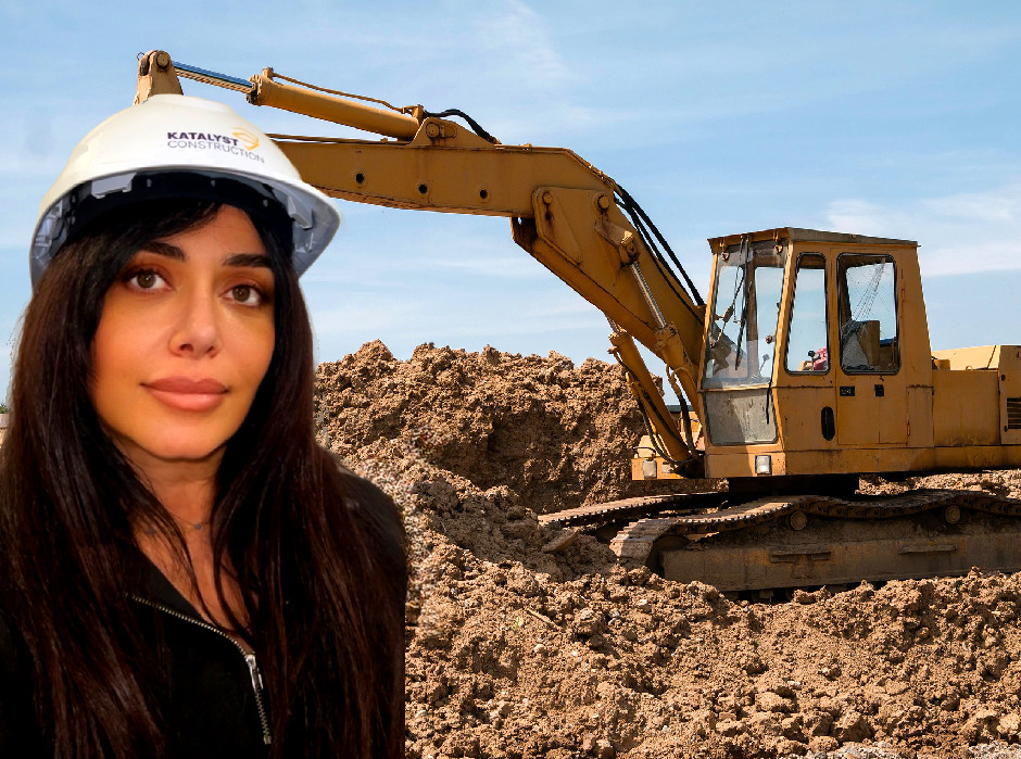 A woman wearing a hard hat stands in front of a large excavator