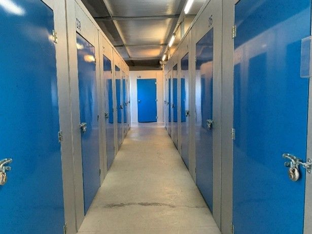 A hallway with multiple blue storage unit doors secured with padlocks inside a storage facility