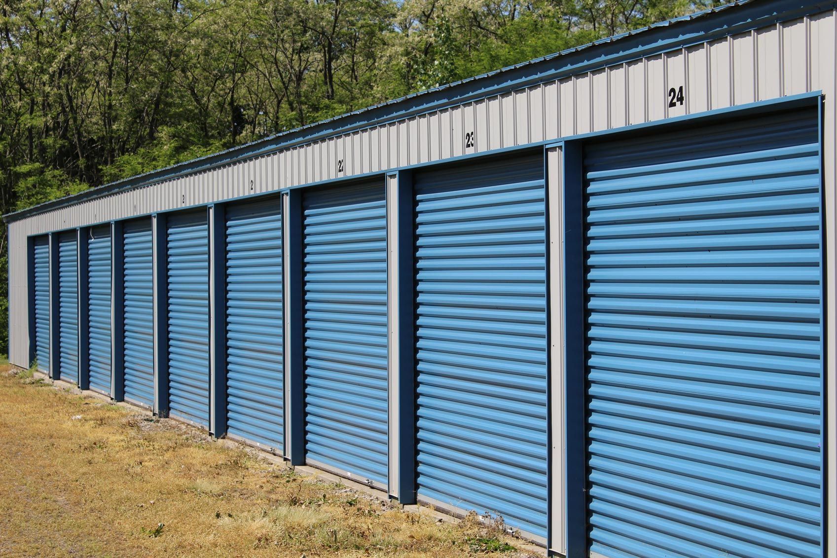 Outdoor self-storage units with blue roll-up doors and numbered signs above each unit. Outdoor self-storage units with blue roll-up doors and numbered signs above each unit.