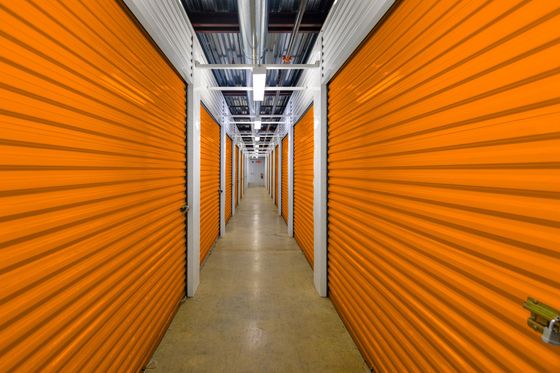 Orange self storage hallway with metal roll-up doors, long corridor lighting, secure units area safe.