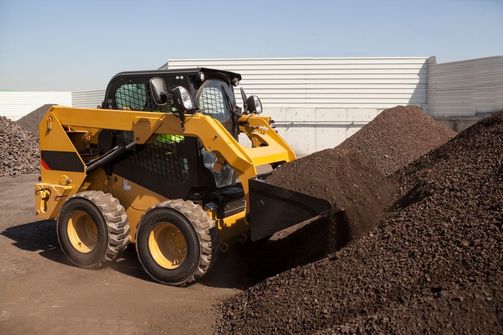 Yellow Skid Steer Loader Pushing Dark Brown Material — Waite Diesel Service in Douglas, QLD