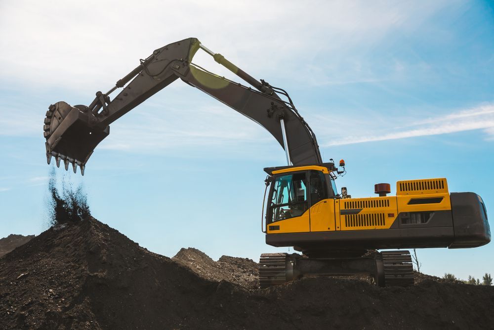Yellow Excavator Dumping Dark Soil Against a Blue Sky — Waite Diesel Service in Douglas, QLD