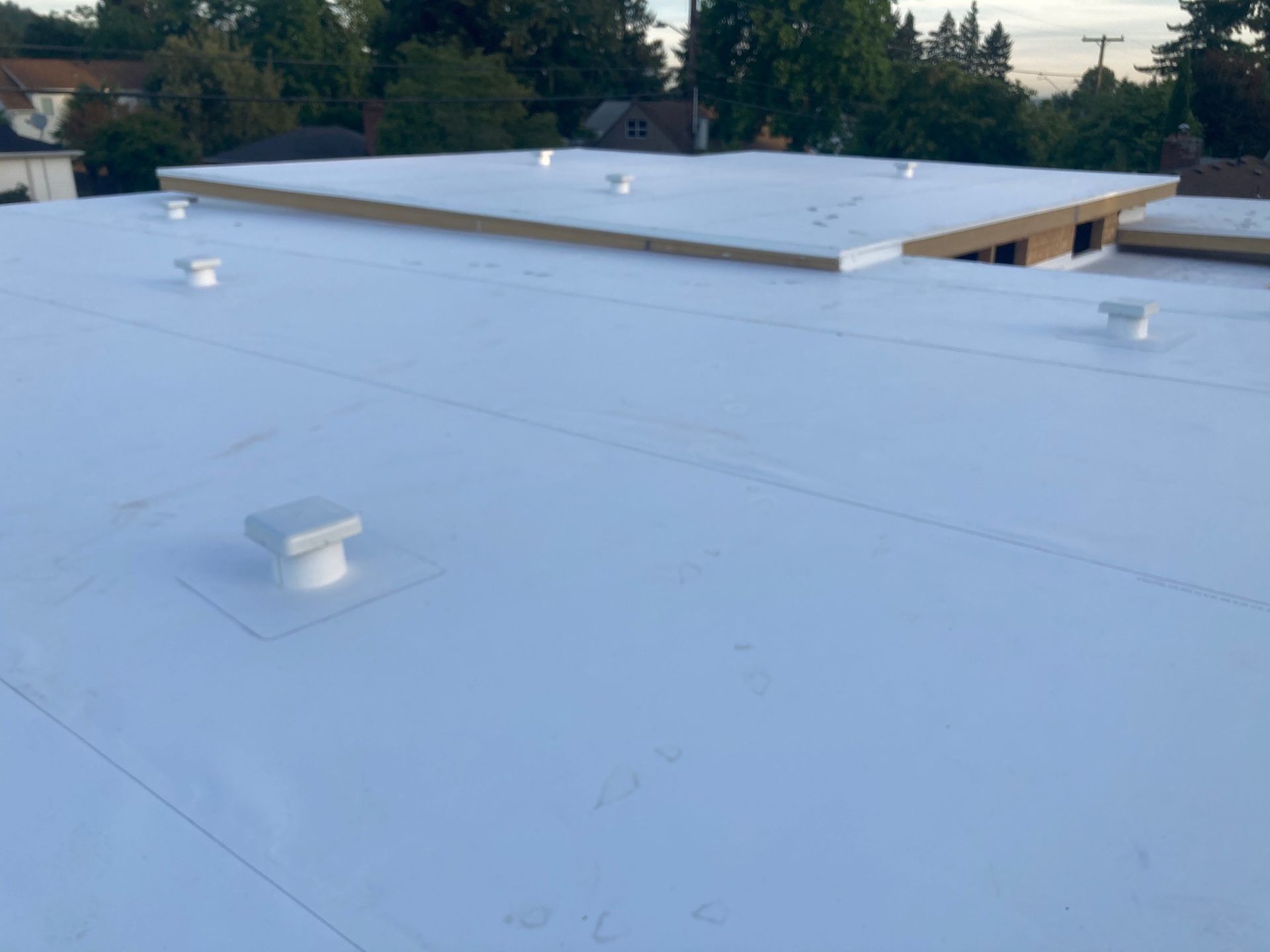 White flat commercial roof with multiple vents and a small structure. White flat commercial roof with multiple vents and a small structure.