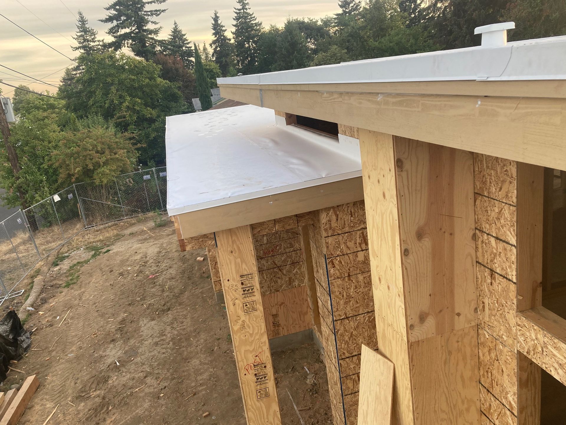 Construction site with wooden framing, white roof, and trees in the background.