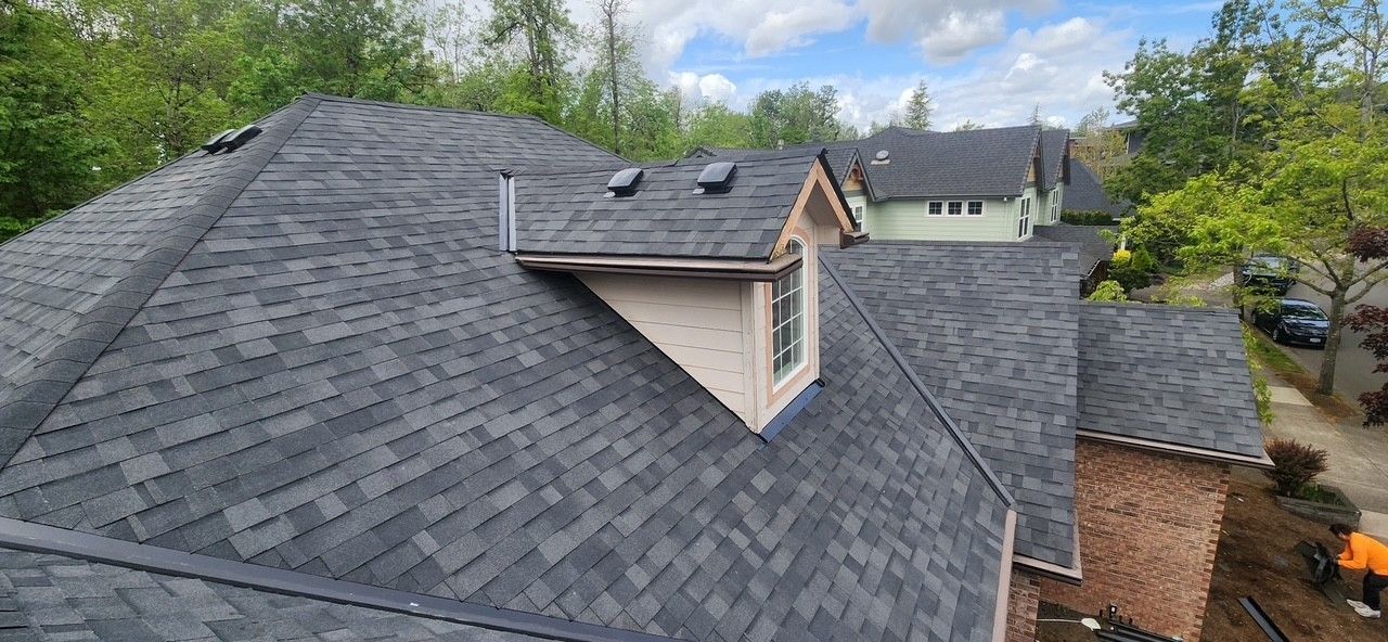 A newly shingled roof with a chimney and small dormer, blue sky above.