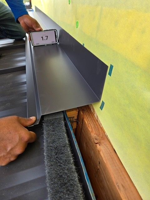 Installing metal flashing on a building. Person holding a level on the flashing above the roof.