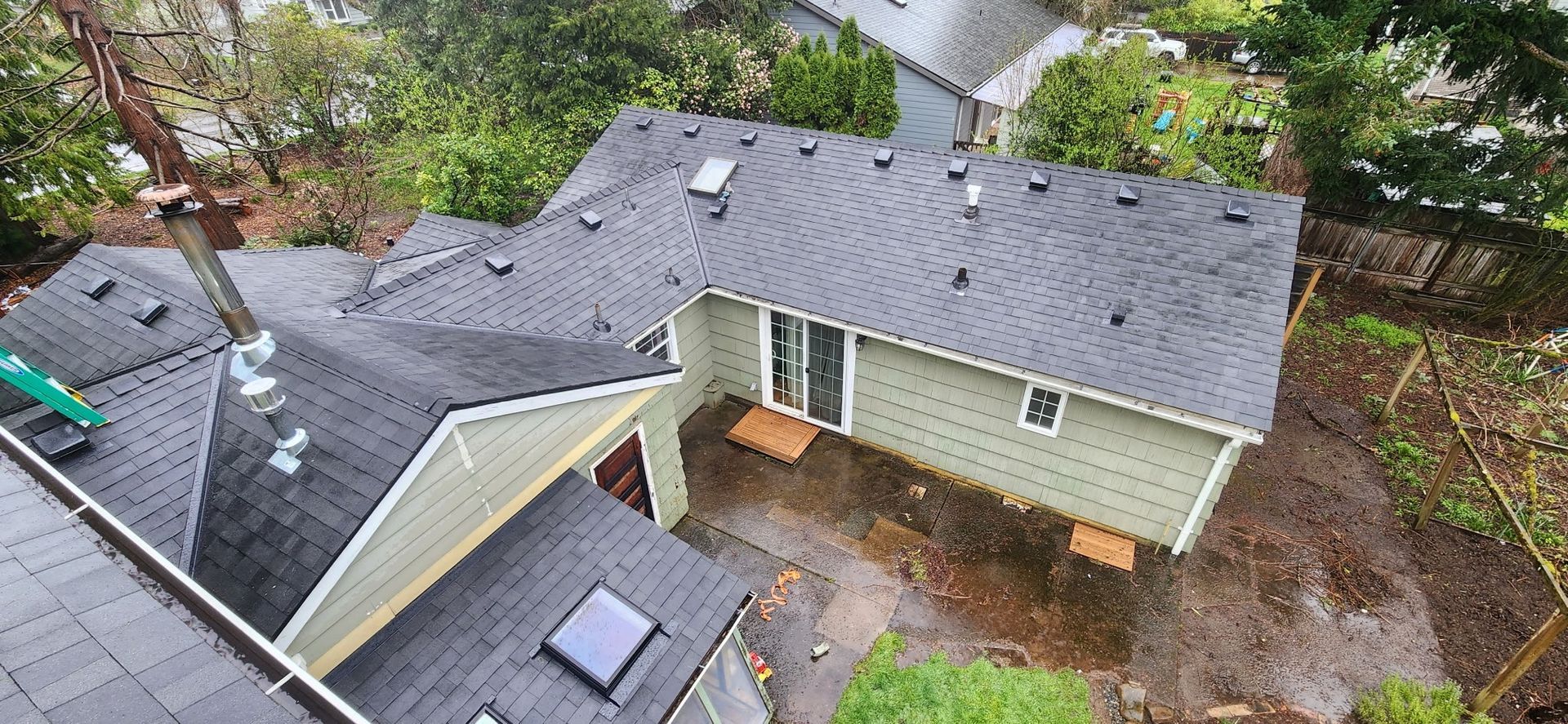 Overhead view of a house with a dark gray roof surrounded by green trees.