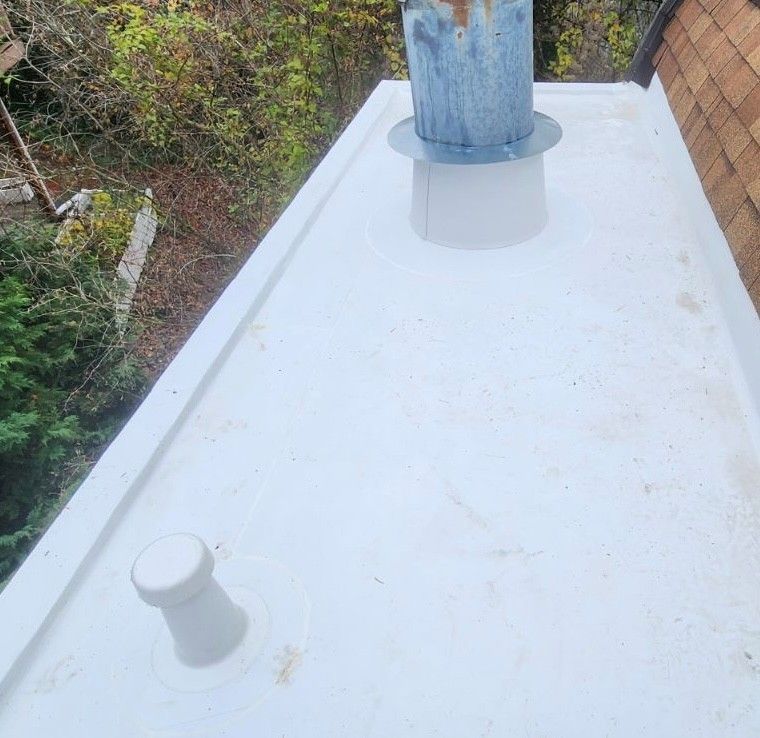White flat roof with chimney and vent pipe. Trees are in background. White flat roof with chimney and vent pipe. Trees are in background.