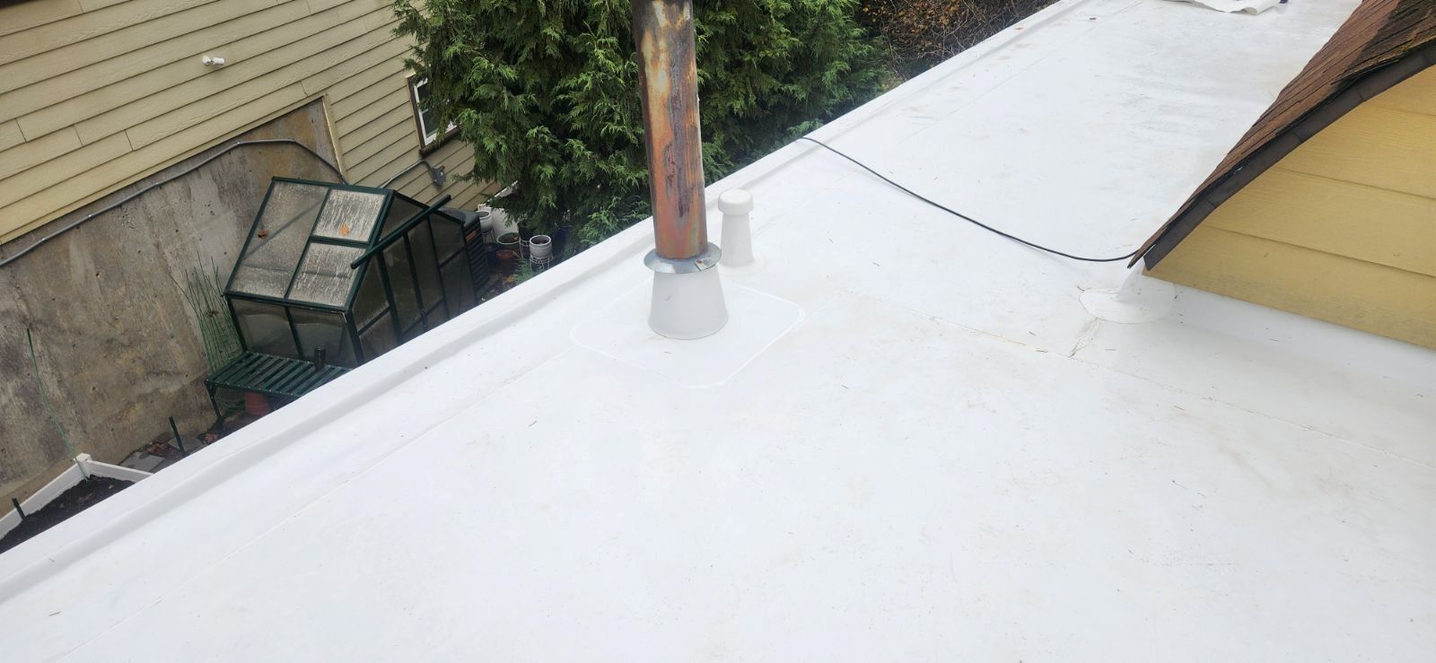 A white flat roof with a copper pipe and a small vent. A metal structure is visible to the left.