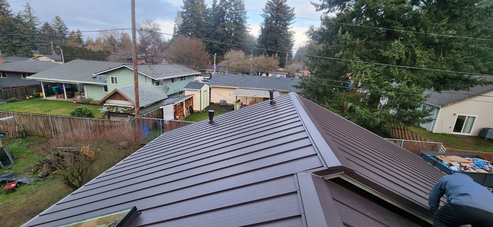 A metal roof on a house in a residential neighborhood with trees in the background.