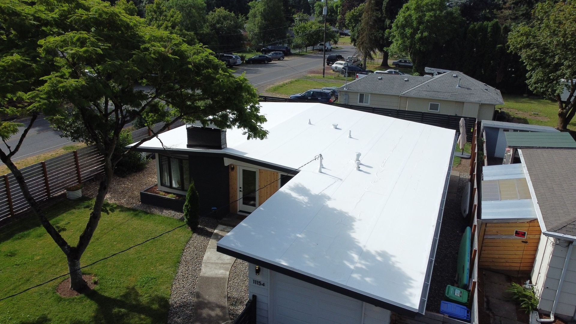 Aerial view of a mid-century modern style home with a white roof and black accents, surrounded by greenery.