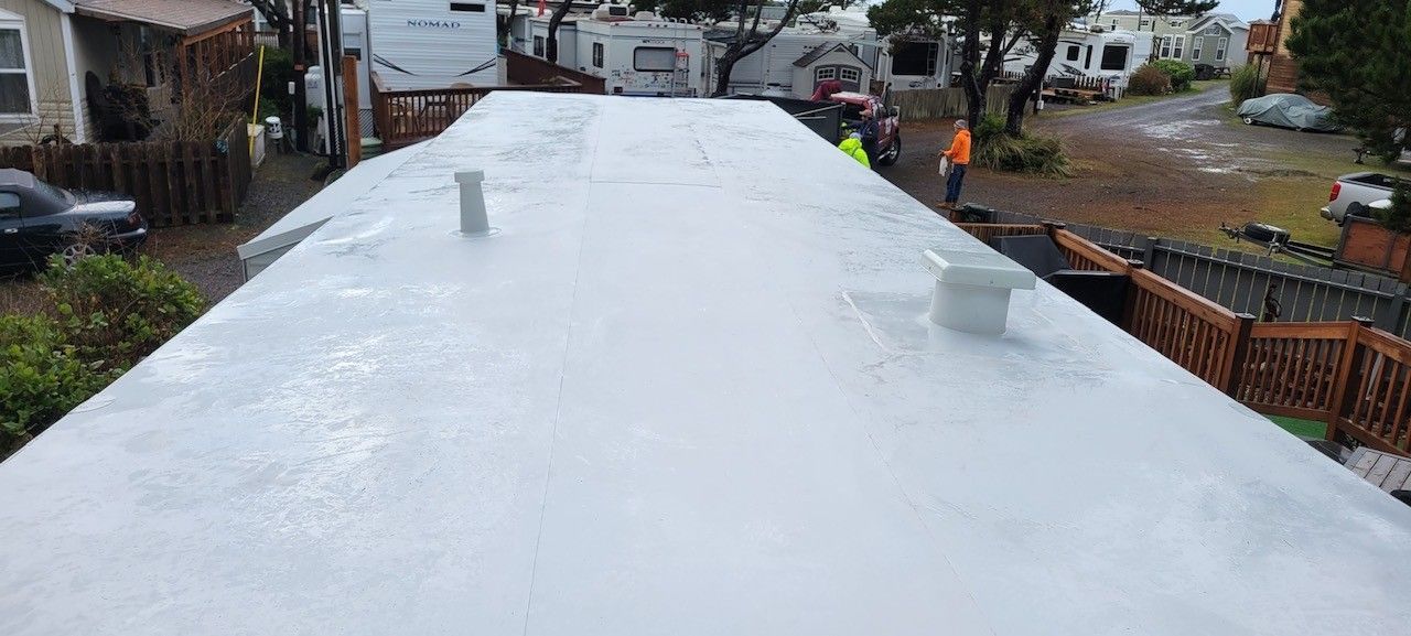 View from a roof of a freshly coated white surface with vent pipes. People in safety vests stand nearby.