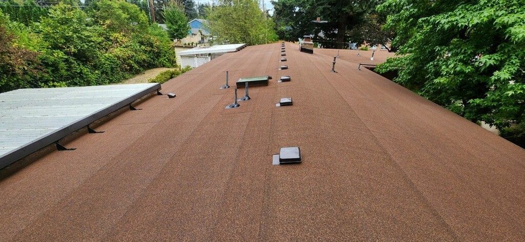 A flat roof with various fixtures, surrounded by green trees, under a bright sky.
