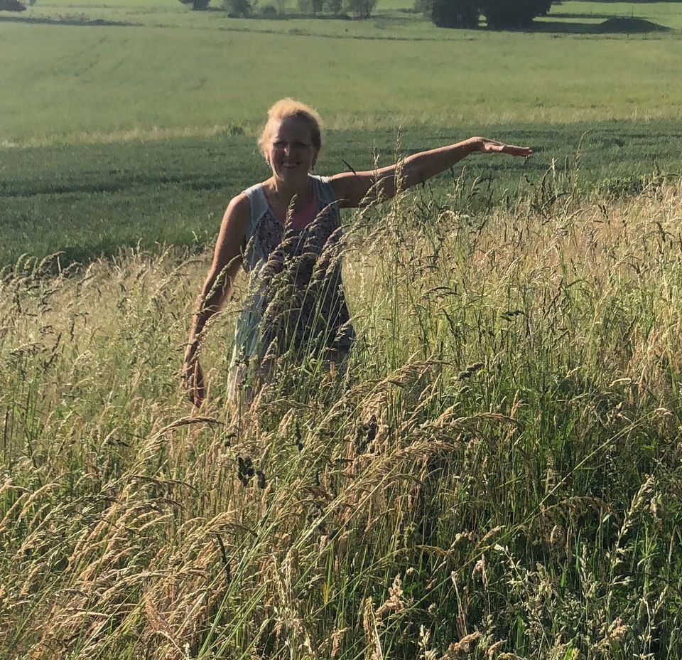 A photo of Viviane standing in a field with outstretched arm to illustrate the grass reaching her shoulder in height.