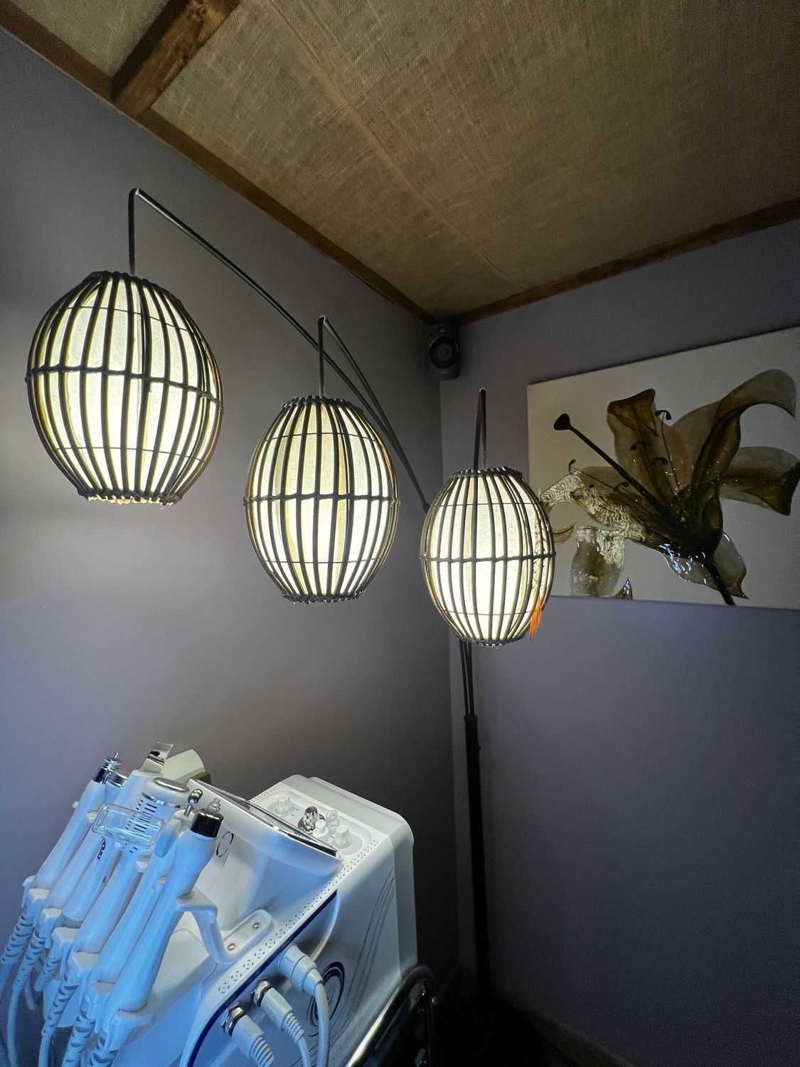 Three globe pendant lights hang over medical equipment in a room with a floral artwork.
