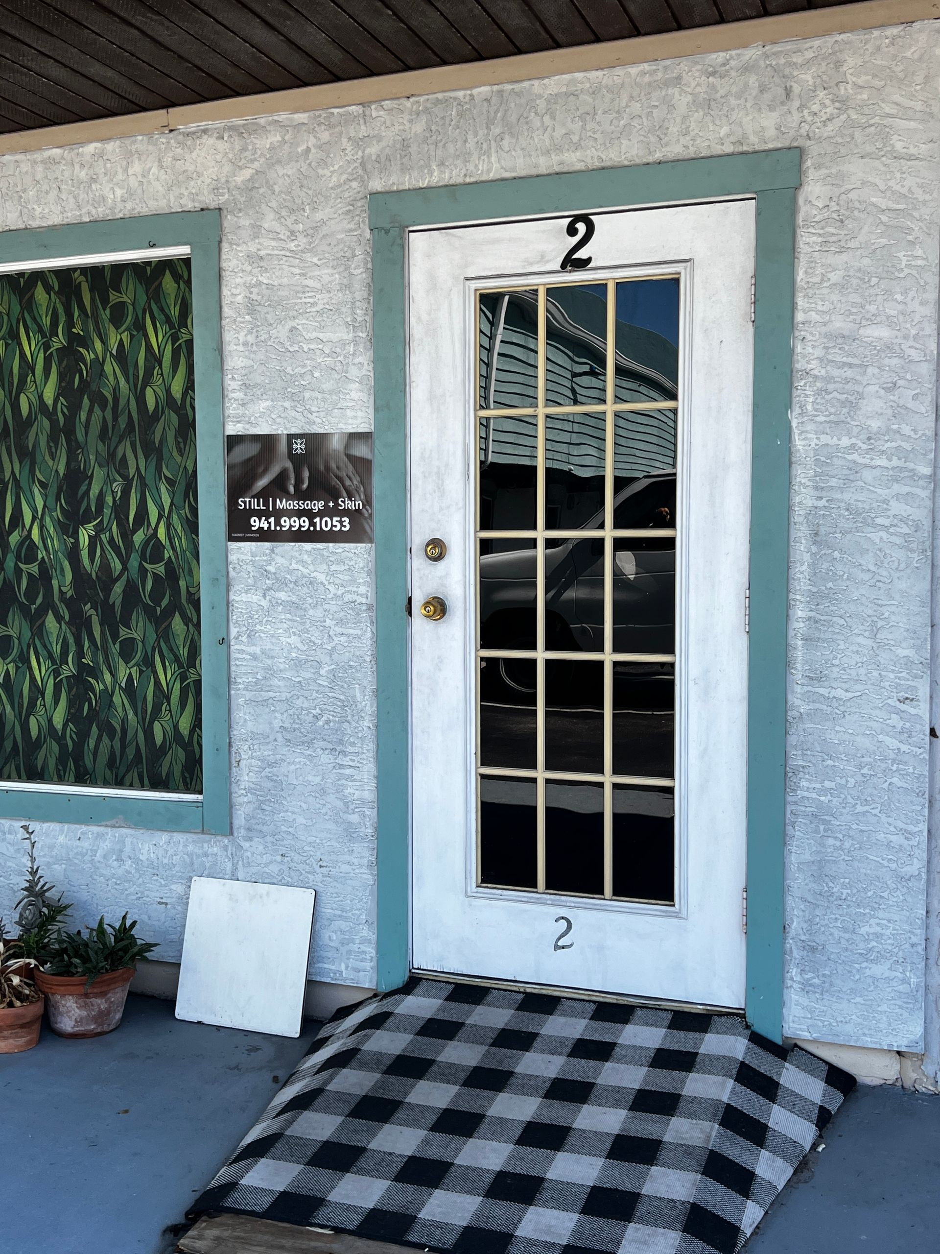 Doorway to unit 2, white door with window, black and white checkered mat, sign