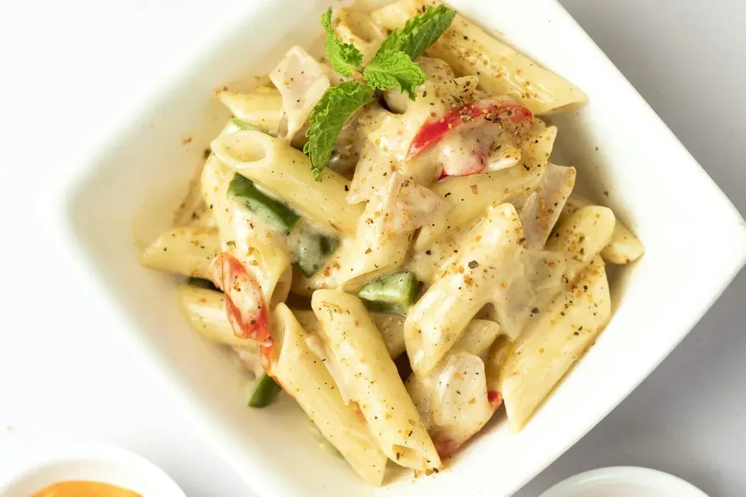 Creamy penne pasta with red and green peppers in a white bowl