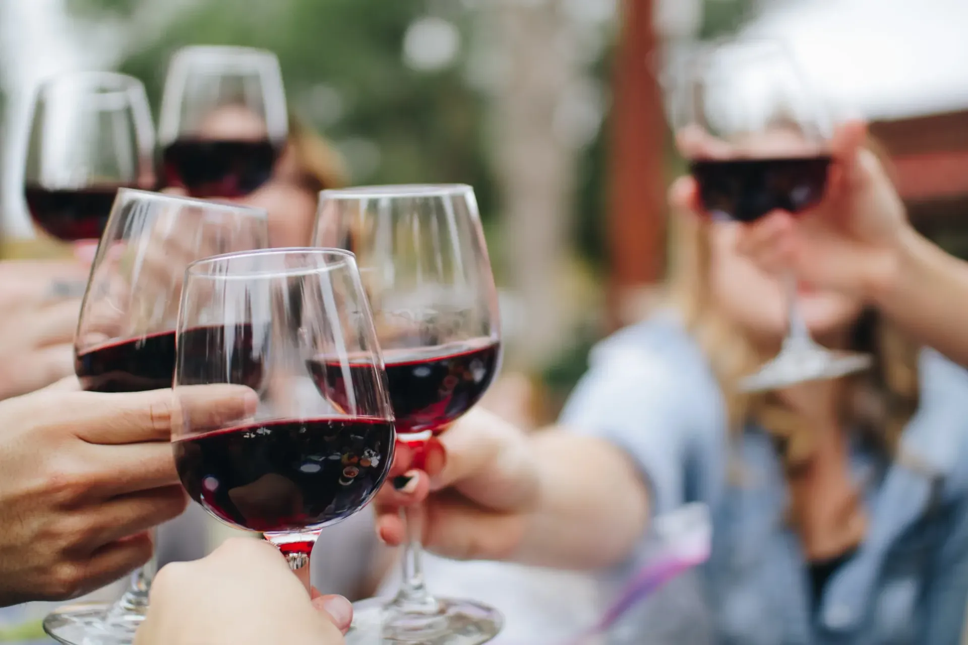 People clinking glasses of red wine at an outdoor gathering