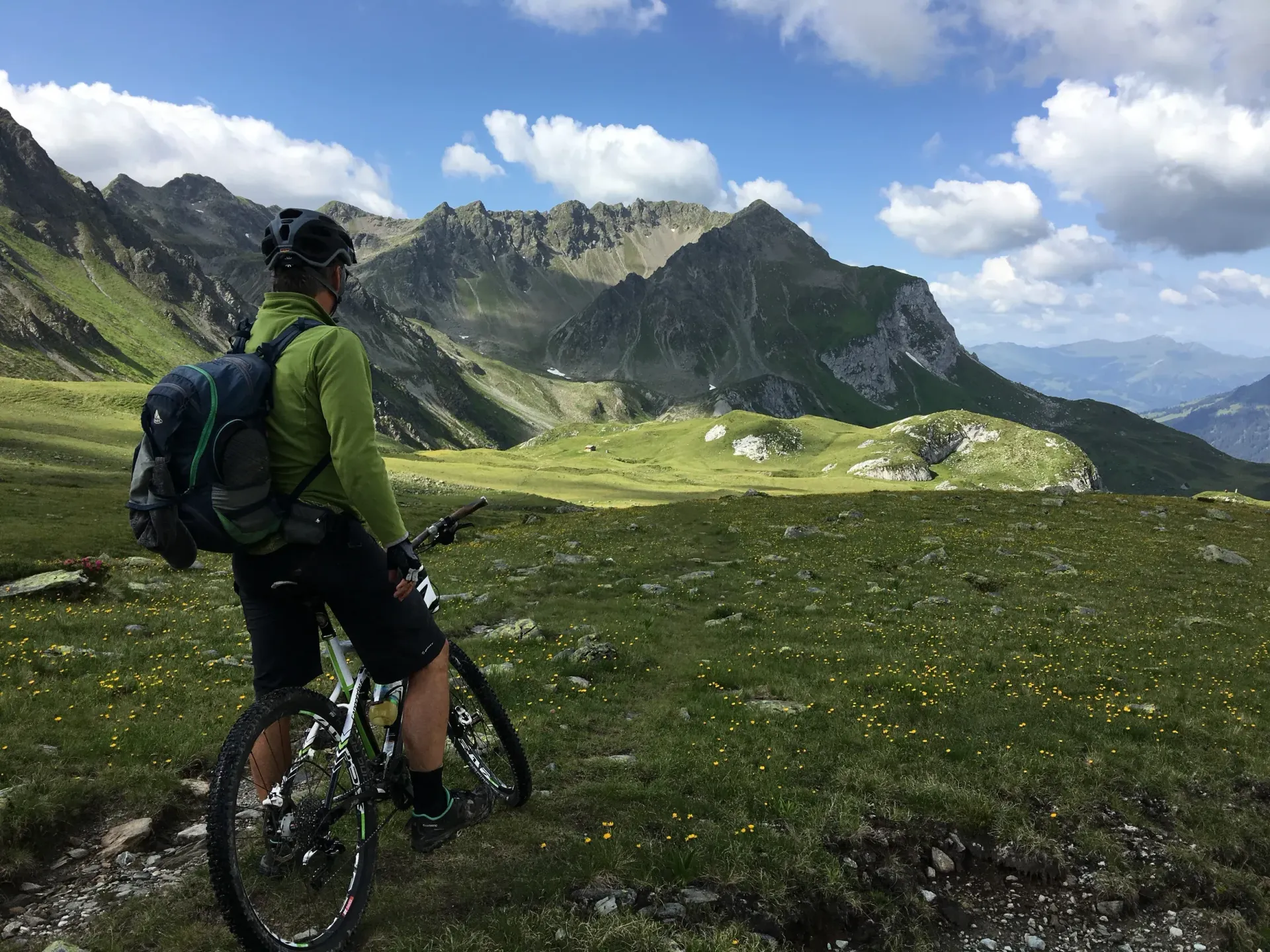 Cyclist with backpack on a mountain trail overlooking green alpine peaks and valleys