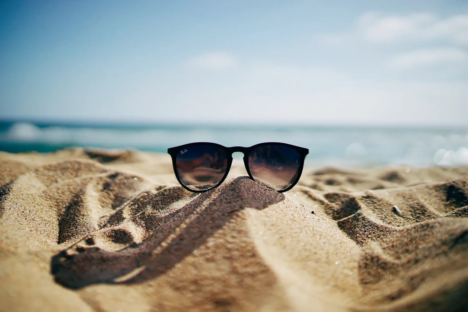 Sunglasses resting in sand on a sunny beach with the ocean in the background