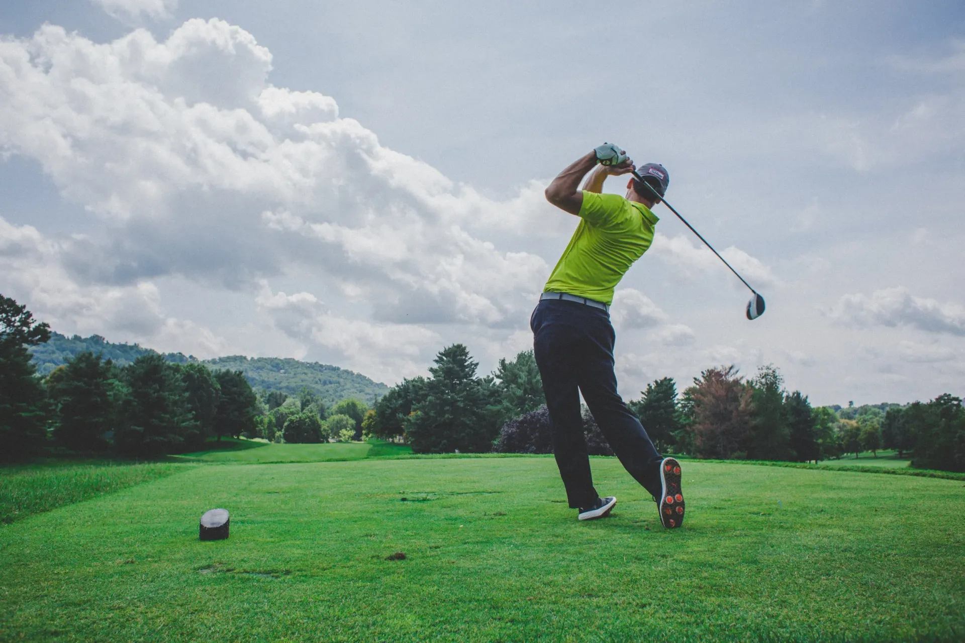Golfer in neon green shirt swinging a club on a lush course under cloudy skies