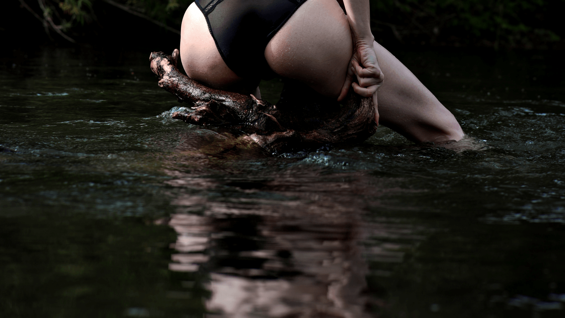 A woman in her underwear sitting on wood in a river.