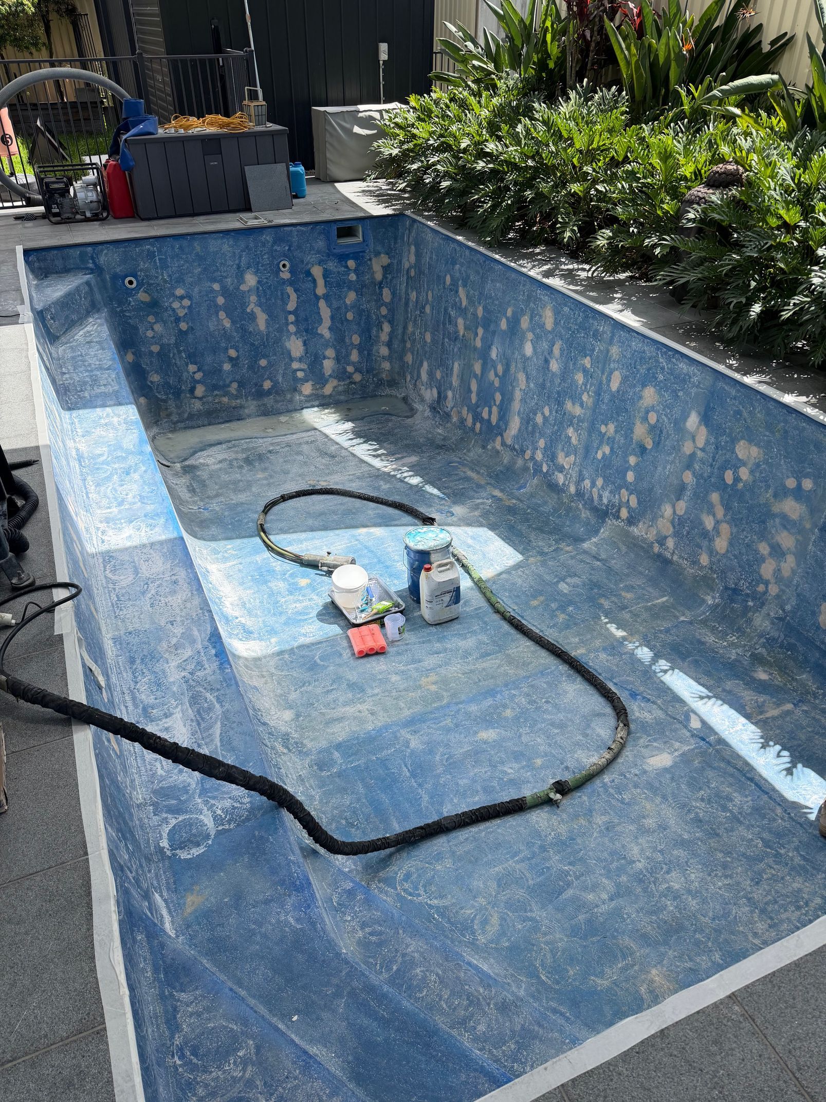 An empty rectangular pool with mottled blue-and-white finish under renovation, with a paint can and hose on the floor. — East Coast Pool Resurfacing In Port Macquarie, NSW