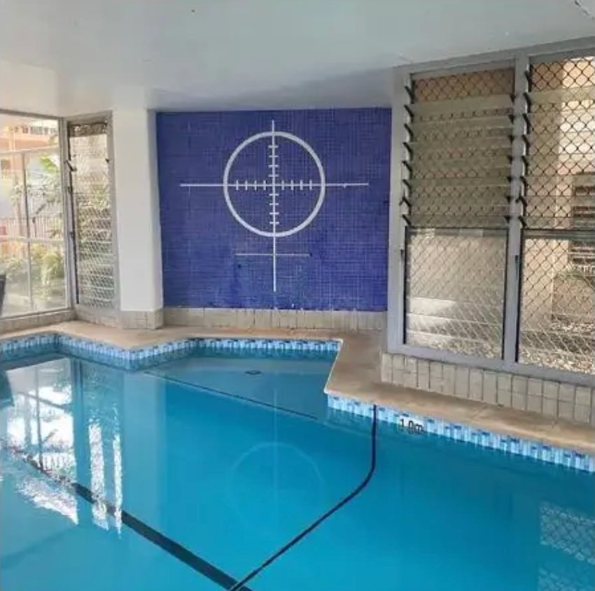 Indoor swimming pool with blue tiles, featuring a white crosshair symbol on the back wall.  — East Coast Pool Resurfacing In Port Macquarie, NSW